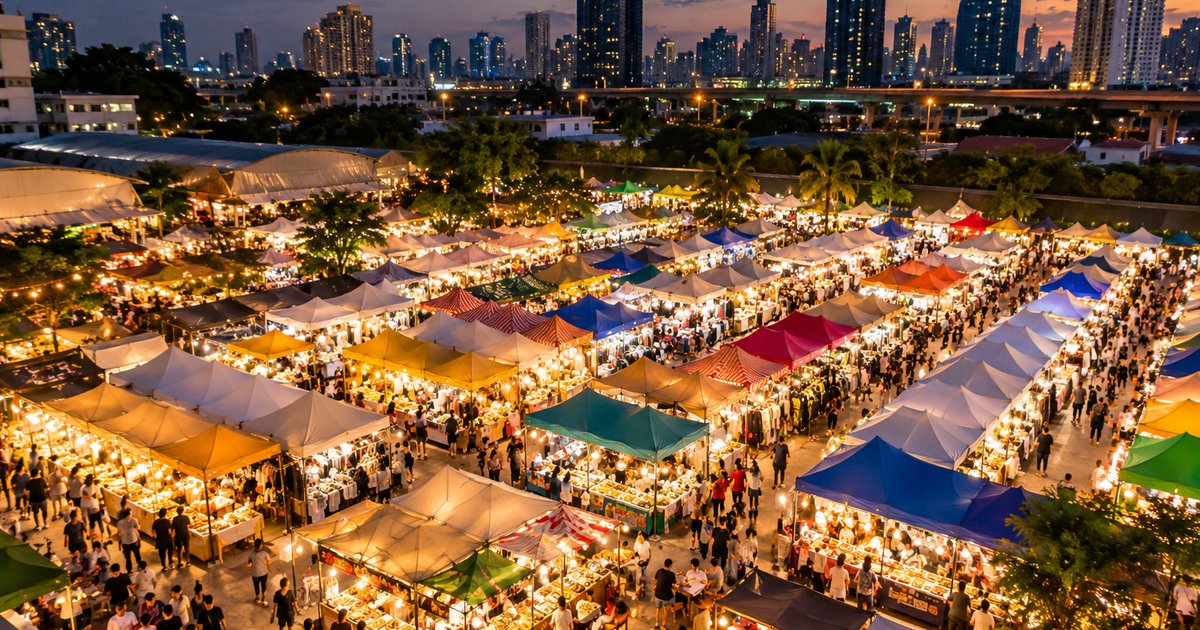 Illustrative view over a Bangkok night market at dusk: colourful food-stall canopies, string lights and the city skyline behind